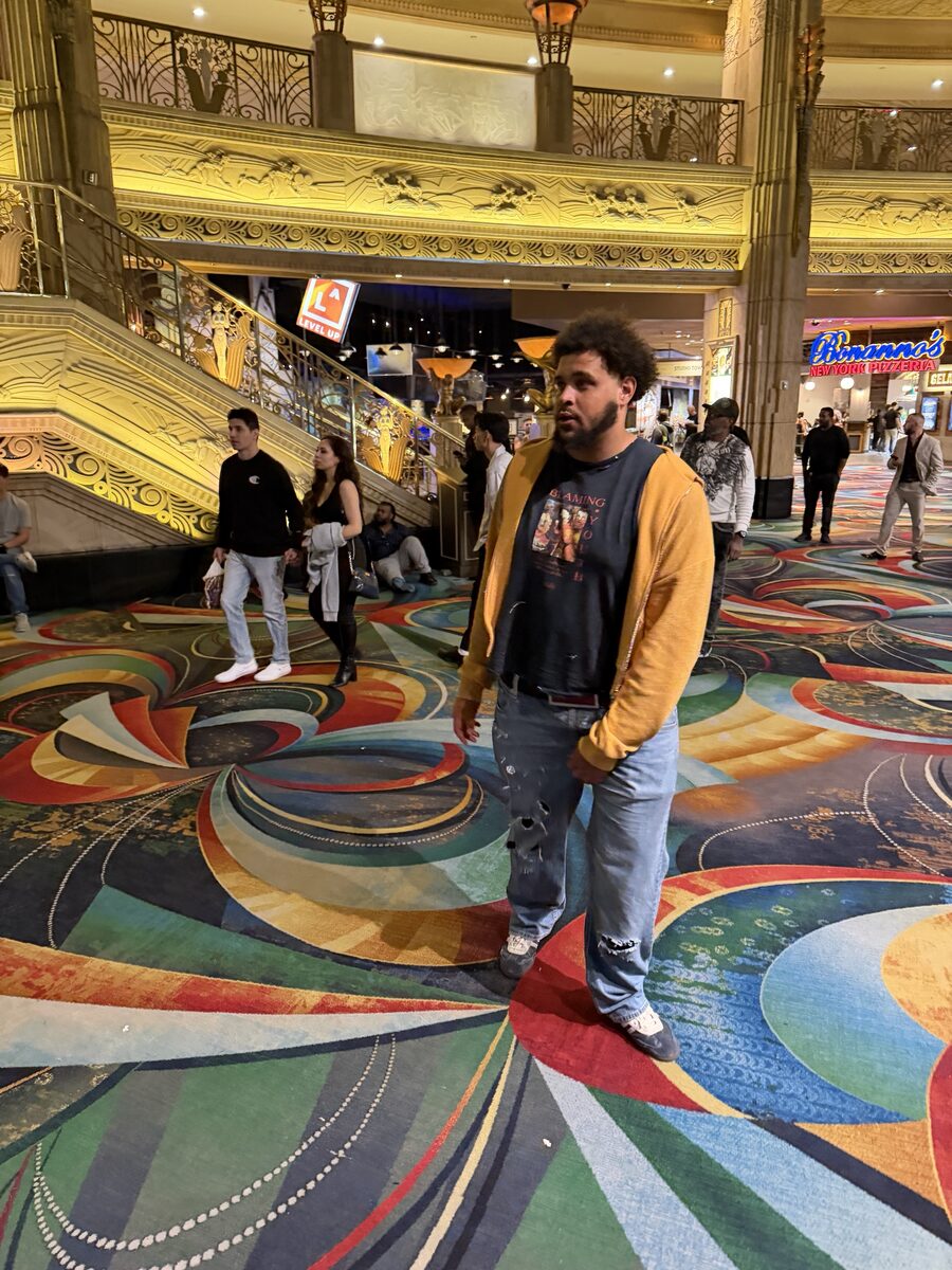 Aura Studioz founder wearing the mustard Aura Zip over a graphic tee and distressed denim inside a Las Vegas casino